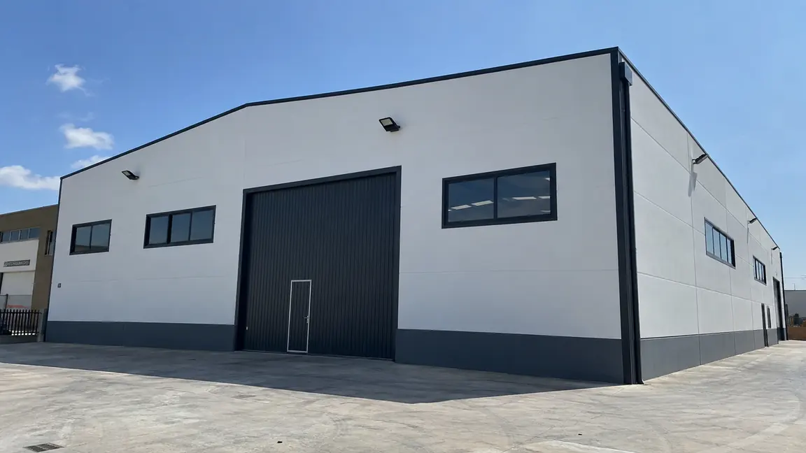 Fachada de una nave industrial pintada por Reformas DLCP en blanco con zócalo gris antracita y portón de carga oscuro