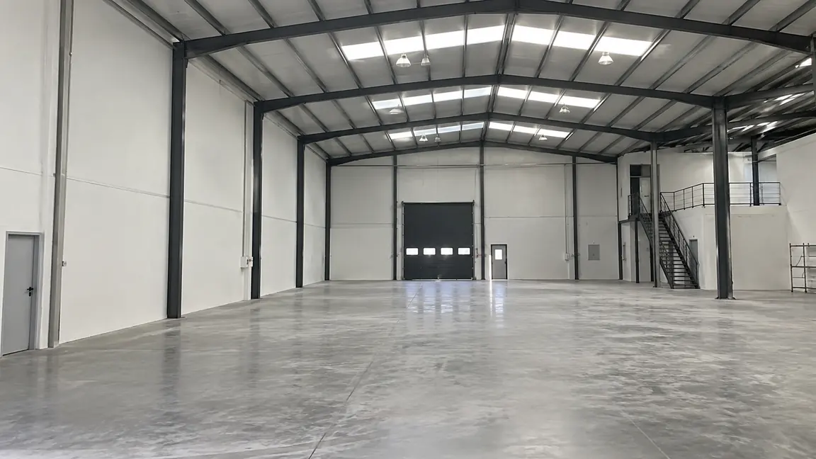 Interior diáfano de una nave industrial pintada por Reformas DLCP, con la estructura metálica en gris oscuro, lucernarios en cubierta y suelo de hormigón
