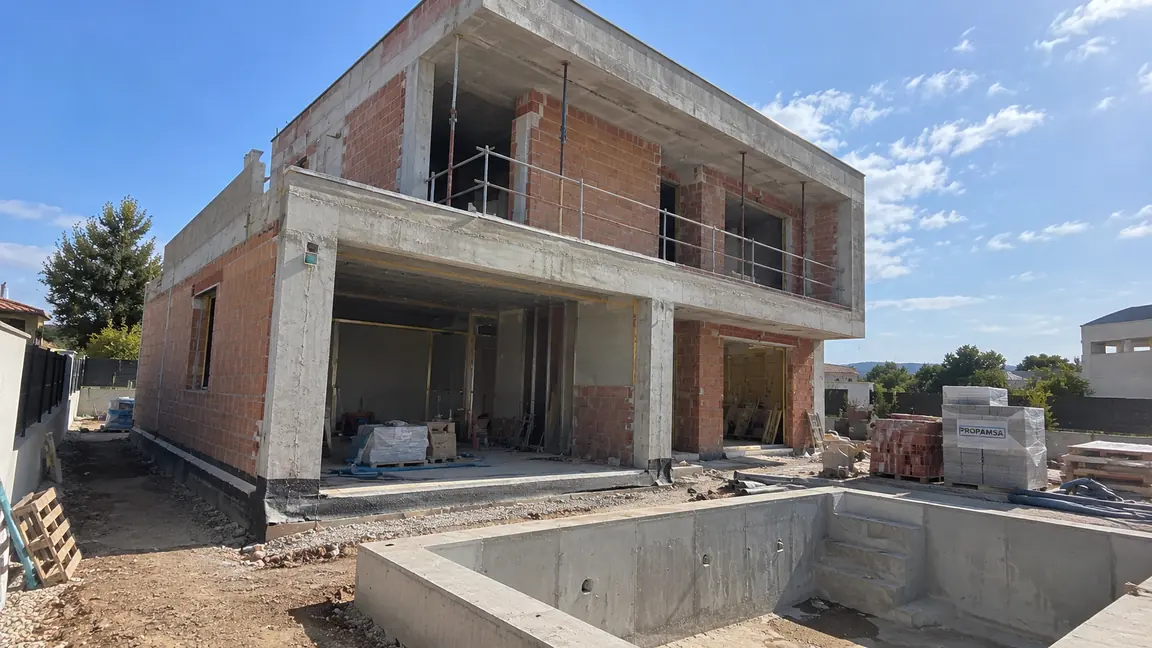 Vivienda unifamiliar en construcción por Reformas DLCP, con la estructura de hormigón y el cerramiento de ladrillo levantados y el vaso de la piscina hormigonado