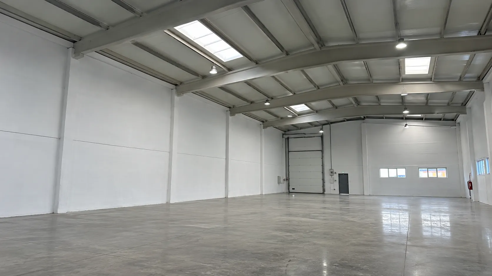 Nave industrial diáfana pintada por Reformas DLCP, con las cerchas y la cubierta en blanco, lucernarios y suelo de hormigón
